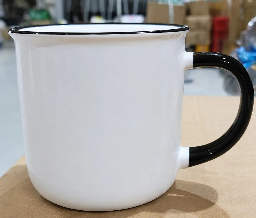 An undecorated white campfire mug with a black rim and handle